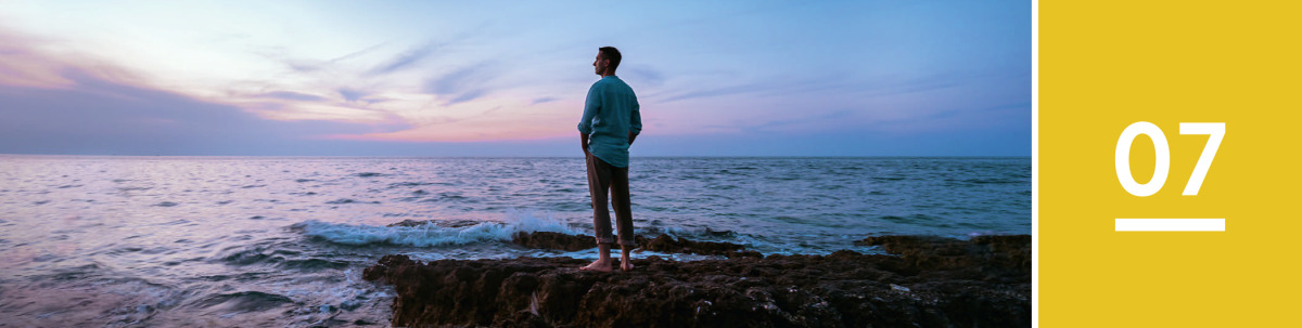 Image 1: A man stands on a rocky shore and looks across the ocean at twilight.