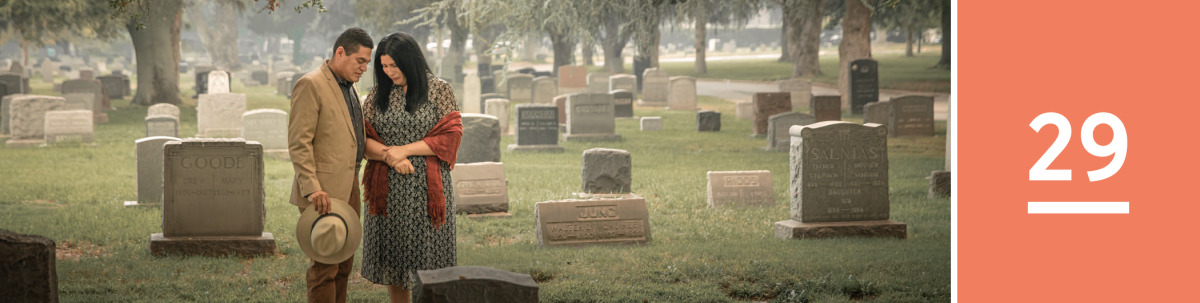 Image 1: A couple prays in front of a headstone in a cemetery.