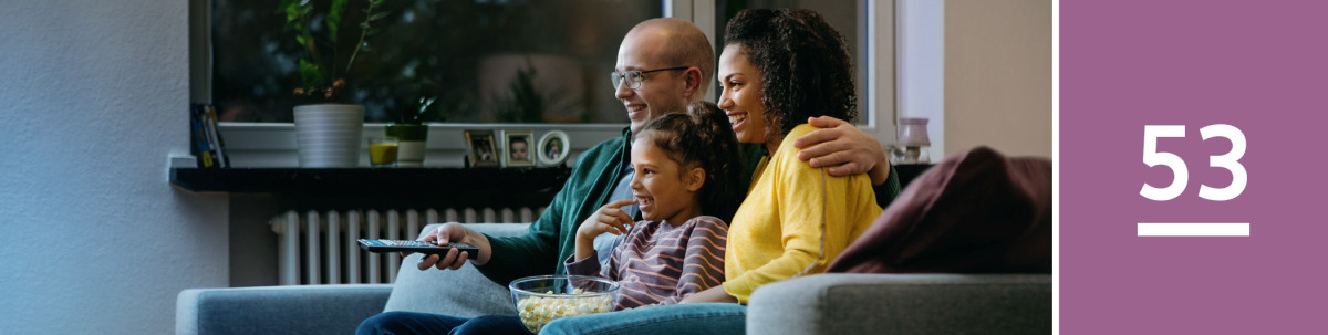 Image 1: A father, mother, and young daughter eat popcorn and watch television.