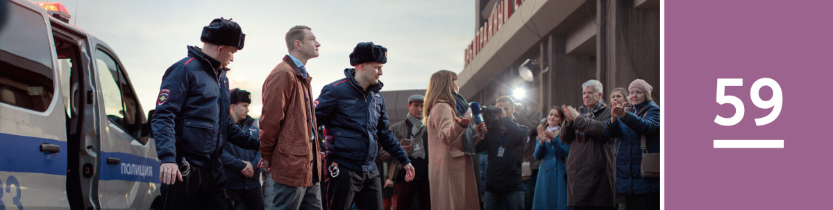 Image 1: Two officers escort a Witness brother in handcuffs past news reporters and fellow Witnesses.