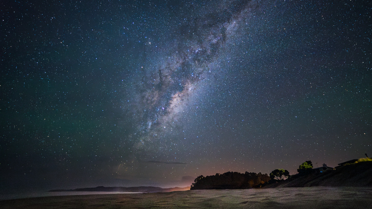 Uma praia com o céu cheio de estrelas.