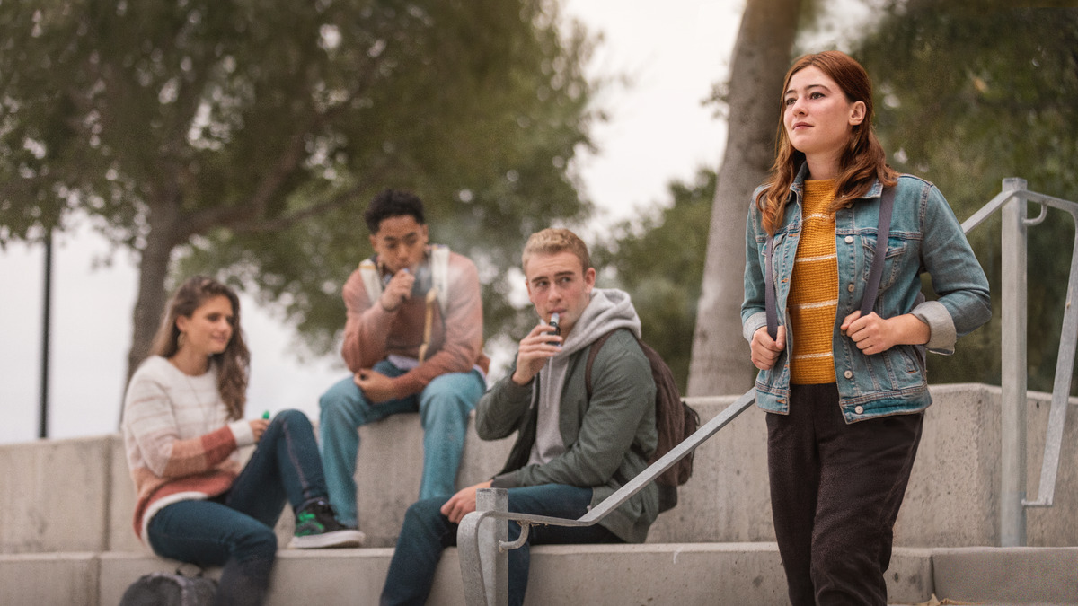 Uma irmã jovem indo embora da escola para casa. Ela passa por alguns colegas de escola que estão fumando cigarros eletrônicos. Os colegas estão observando a irmã, mas ela está olhando para frente com confiança.