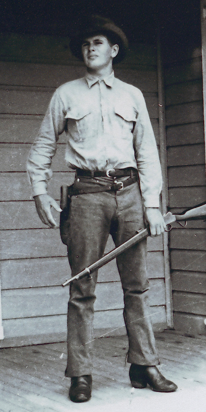 IMAGE 2: A black-and-white photograph of young Allan holding a rifle.