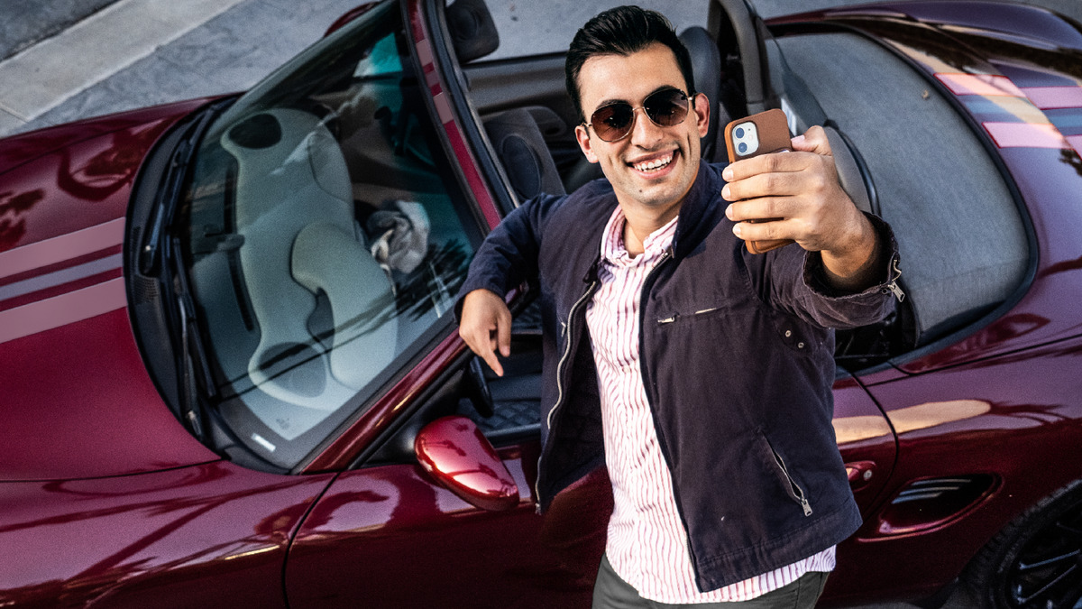 Irmão posando para uma selfie ao lado de um carro esportivo de luxo.